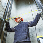 machinist worker measure and adjusting elevator construction with in lift shaft